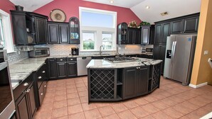 A kitchen with dark cabinetry, a central island, a large window, and a view of a house outside. - OCEANFRONT, priv pool & Hot Tub, Rec Room-WL1011, Sea Esta (Corolla)