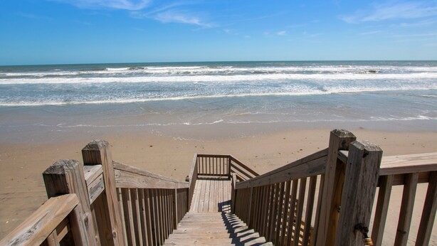 Un escalier en bois menant à une plage, avec des vagues en arrière-plan.