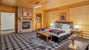 A log cabin bedroom with a stone fireplace, a bed with a plaid bedspread, a bench, and a nightstand with a lamp. - Abode at Black Bear #330, hot tub, pool table, steps to Deer Valley (Park City)