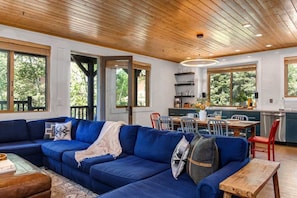 A modern living room with a blue sofa, wooden ceiling, and large windows.