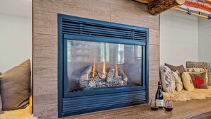A fireplace with logs, a bottle of wine, and two glasses on a wooden surface. - Abode at Black Bear #330, hot tub, pool table, steps to Deer Valley (Park City)