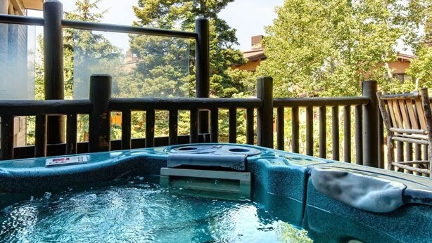 A hot tub with a wooden deck and railings, surrounded by trees. - Abode at Black Bear #330, hot tub, pool table, steps to Deer Valley (Park City)