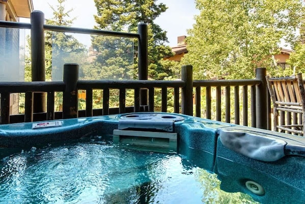 A hot tub with a wooden deck and railings, surrounded by trees.