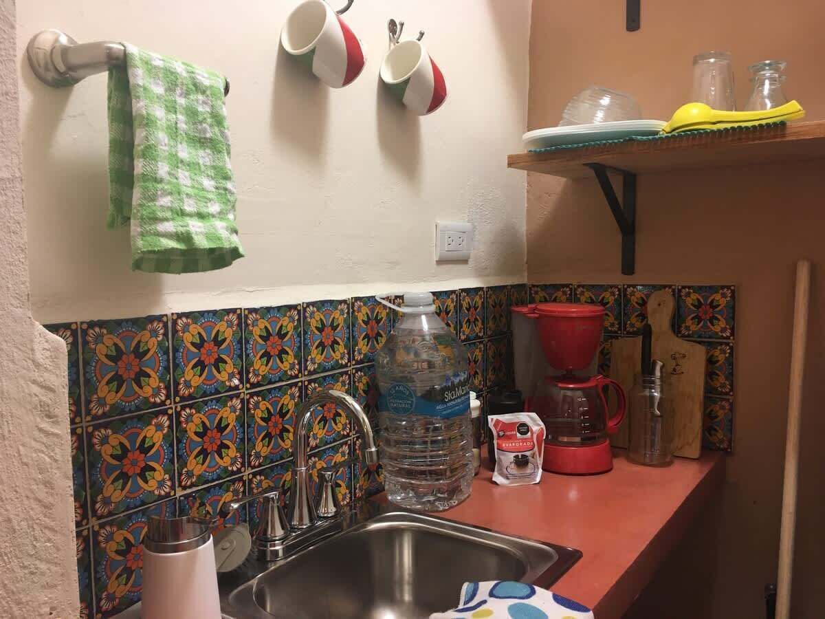 A kitchen with a sink, faucet, and a water dispenser. There are colorful tiles on the backsplash and a green towel hanging on the wall.