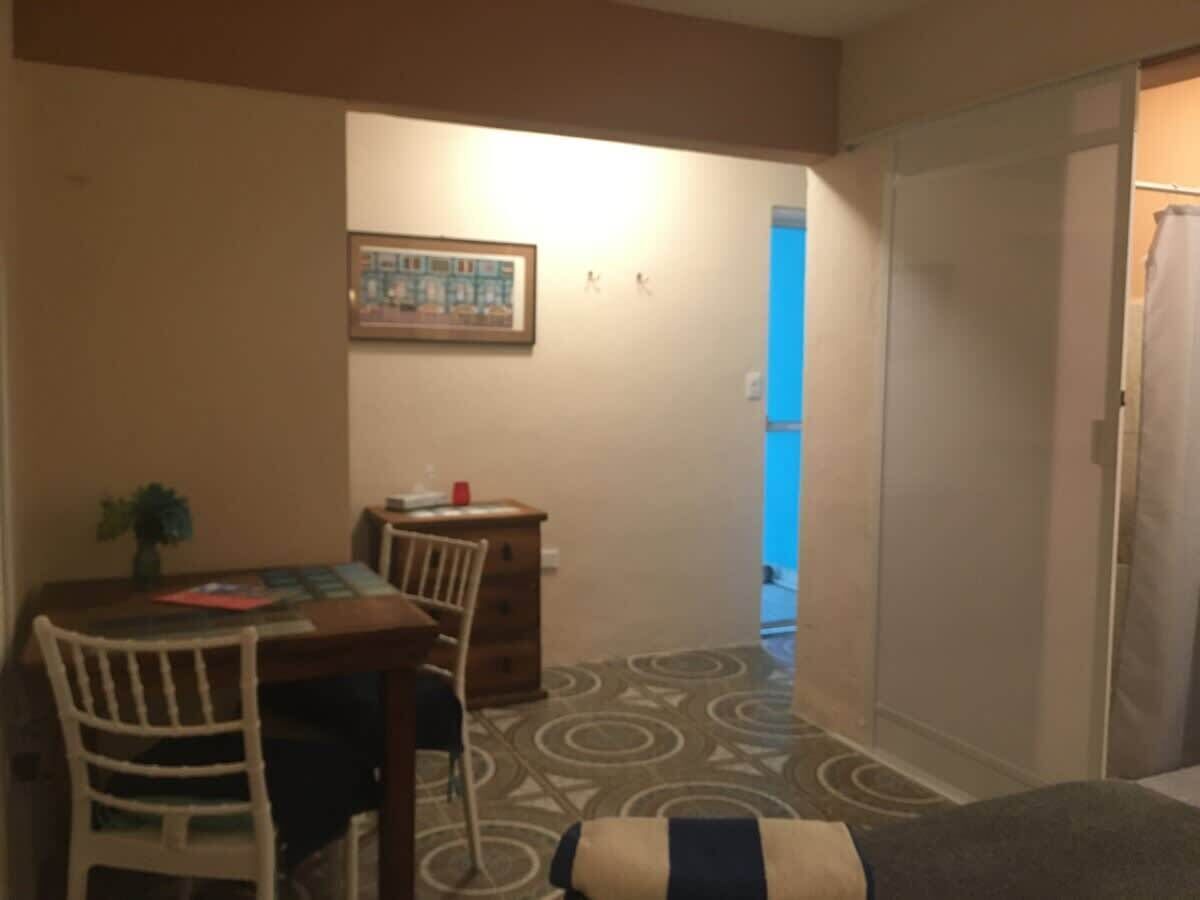 A small room with a dining table, two chairs, a small cabinet, and a patterned carpet.