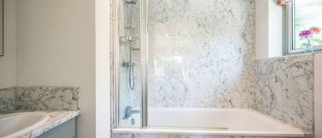 A bathroom with a glass-enclosed shower, a bathtub, and marble walls.