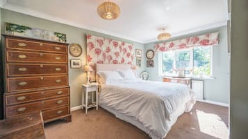 Une chambre avec une grande commode en bois, un lit avec une literie blanche, une table de chevet, une lampe et une fenêtre avec des rideaux.