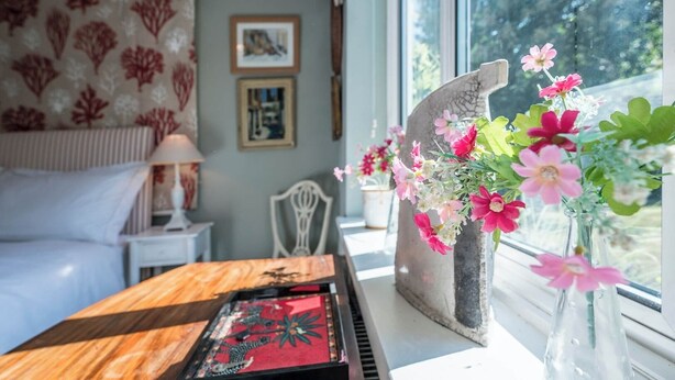 A room with a bed, a desk with a decorative tray, a vase with flowers, and a window with a view of trees. - NO 108, private room in Aldeburgh (Aldeburgh)