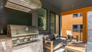 An outdoor kitchen with a grill, a sofa, and a wooden table.