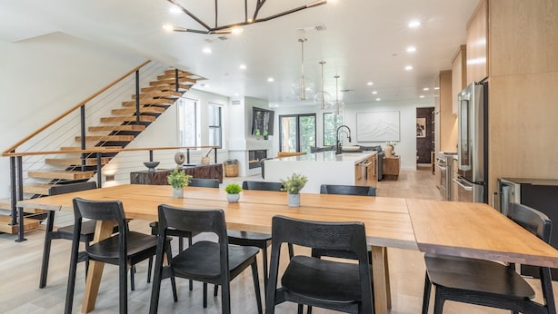 A modern kitchen with a wooden island, black chairs, and a staircase.