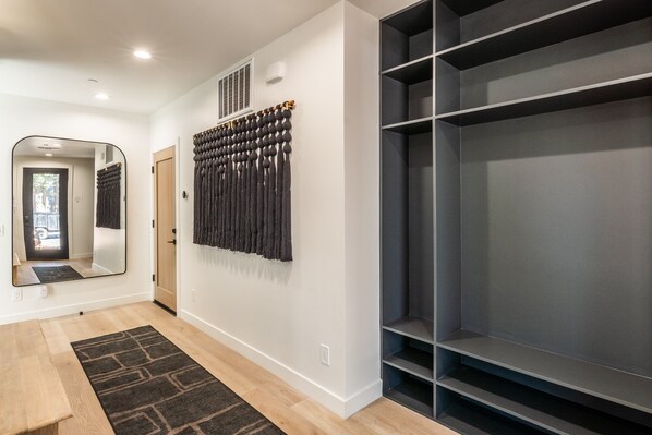 A hallway with a wooden bench, a dark patterned rug, a mirror, and a wall-mounted storage unit. - New Luxury 4BR /3BA Obsidian Reserve #126 – Private Hot Tub & Sauna, 2-Car Garage, gr8 Views! (Mammoth Lakes)