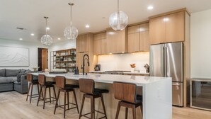 A modern kitchen with wooden cabinets, a stainless steel refrigerator, and a central island with bar stools.