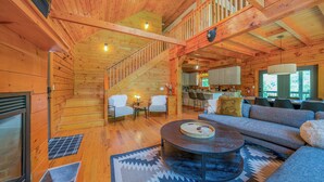 Interior espacioso de una cabaña de madera, con escalera, zona de comedor y sala de estar con sofá y mesa de centro.
