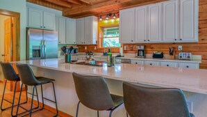 Una cocina moderna con armarios blancos, una isla grande con taburetes de bar, electrodomésticos de acero inoxidable y vigas de techo de madera.
