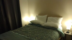 A neatly made bed with patterned bedding, a bedside lamp, and a curtain partially drawn.