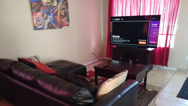 A living room with a black leather sofa, a coffee table, and a flat-screen TV.