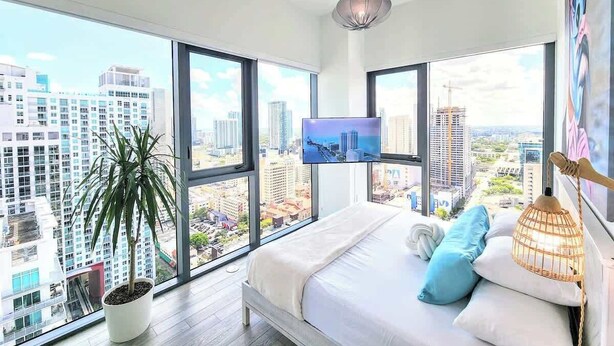 A modern bedroom with a large bed, a TV, and a city view.