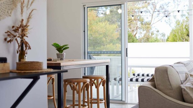 Una cocina moderna con una mesa de madera, taburetes de bar y una planta en maceta.