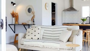Una sala moderna con un sofá, un comedor con una mesa y una cocina con estufa y armarios.