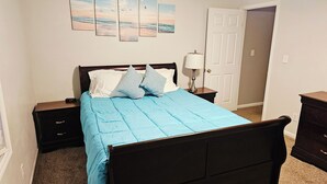Un dormitorio con cama, mesitas de noche, lámpara y puerta.