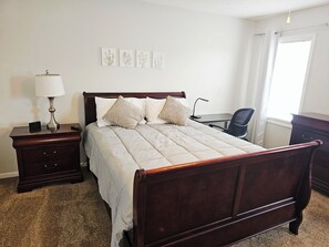 A neatly arranged bedroom with a wooden bed, bedside tables, a lamp, and a desk.