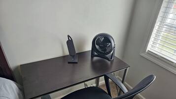 Un petit bureau en bois foncé, avec un ventilateur noir et une chaise noire.