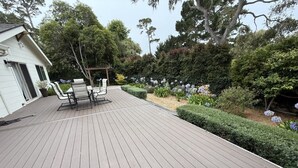 Une terrasse en bois agrémentée d’une pergola et de mobilier d’extérieur, entourée de jardins et d’arbres bien entretenus.