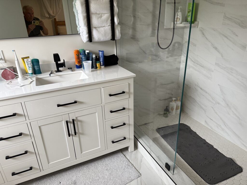 Un baño moderno con tocador blanco, cabina de ducha de vidrio y artículos de aseo en el lavabo.