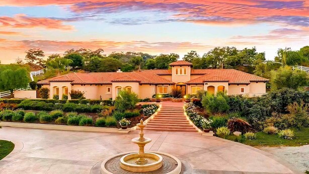 A large, two-story building with a tiled roof, surrounded by landscaped gardens and a central fountain.