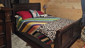 A wooden-paneled bedroom with a bed, a nightstand, a lamp, and a framed picture on the wall.