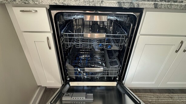 Un lavavajillas abierto en una cocina con gabinetes blancos y encimera de granito.