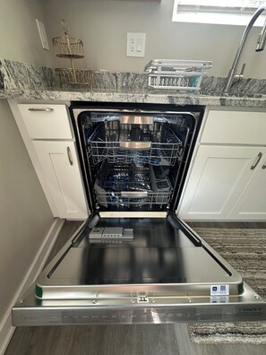 An open dishwasher in a kitchen with white cabinets and a granite countertop.