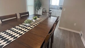 Un comedor con una larga mesa de madera, sillas, un ventilador de techo y vista a la cocina.