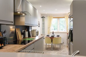 Een kleine keuken met moderne apparaten, een eettafel met gele stoelen en een raam met gordijnen.