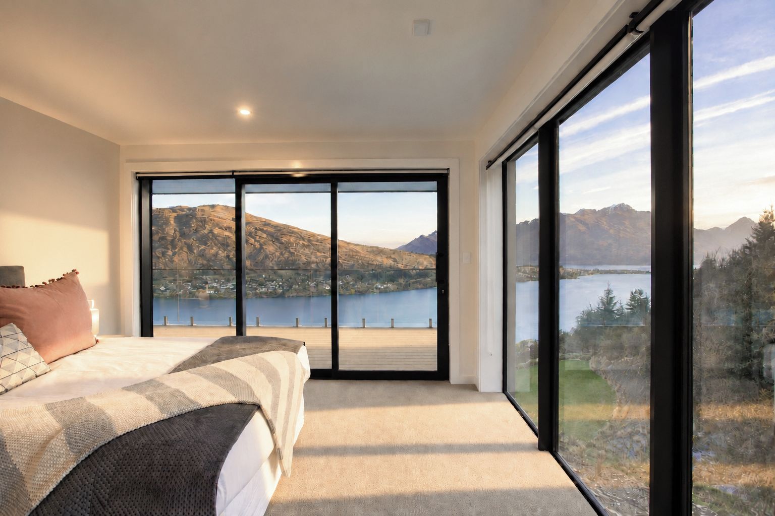 Een slaapkamer met een grote schuifglazen deur die leidt naar een balkon met uitzicht op een meer.