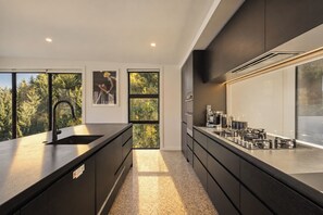 A modern kitchen with a large island, stainless steel appliances, and a view of trees through large windows.