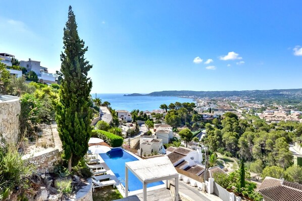 A pool area with a view of the sea, surrounded by greenery and buildings.