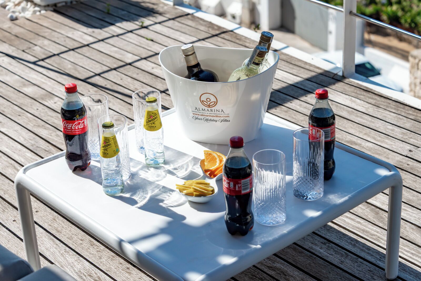 Uma mesa com diversas bebidas e um balde rotulado 'Almaria' em um deck de madeira.