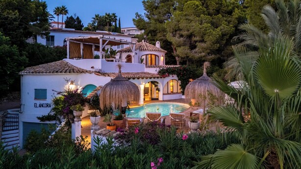 A villa with a swimming pool, surrounded by lush greenery and palm trees.