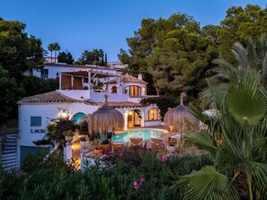 A villa with a swimming pool, surrounded by lush greenery and palm trees.