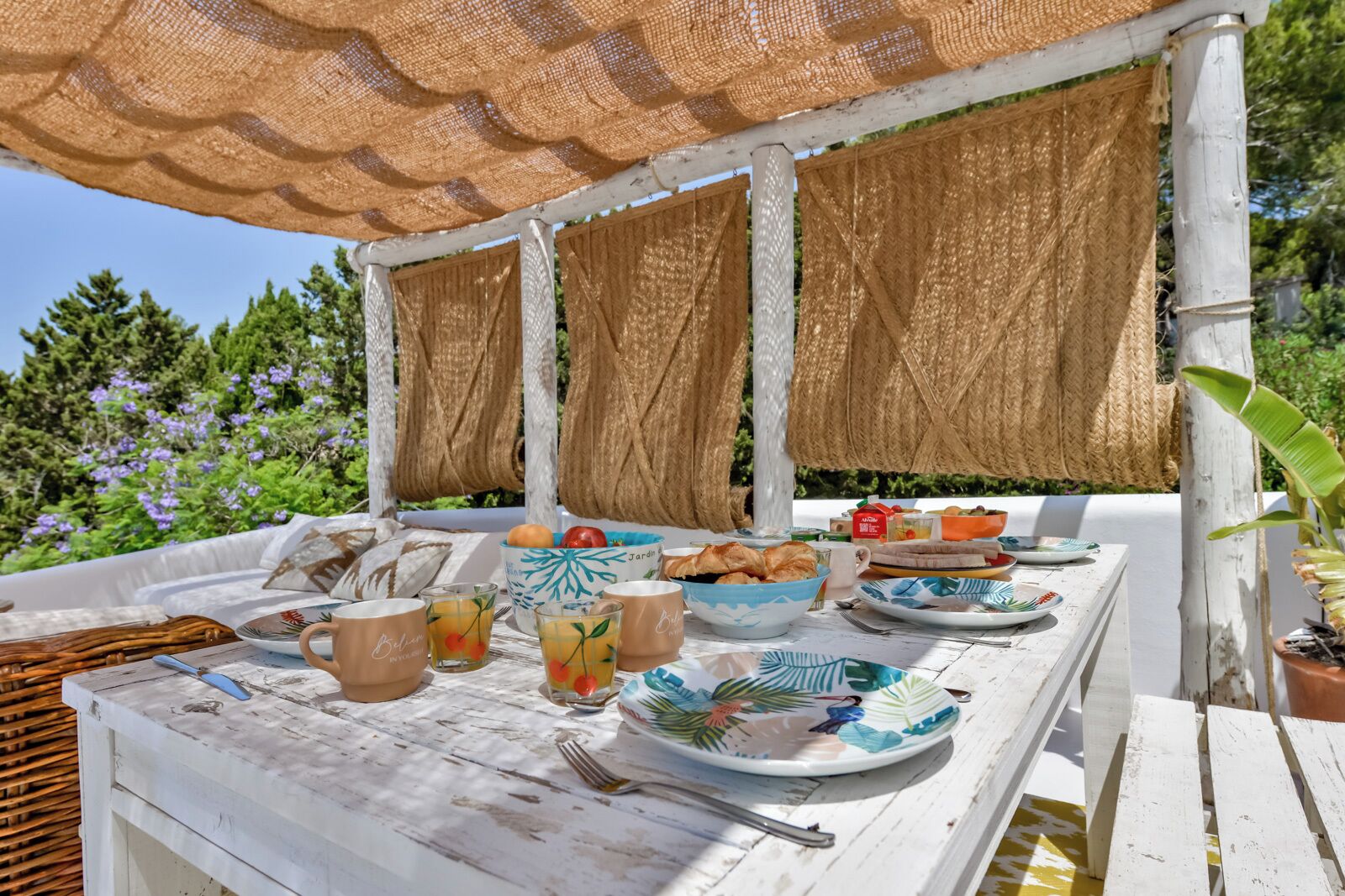 Un espace de restauration en plein air avec une table blanche dressée pour le petit-déjeuner, comprenant des assiettes, des bols et des tasses.