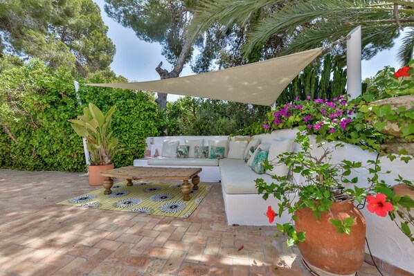 A patio with a white sofa, a wooden table, and potted plants.