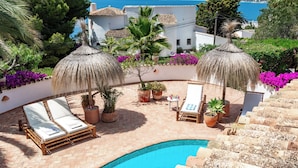 A poolside area with two sun umbrellas, lounge chairs, and potted plants.