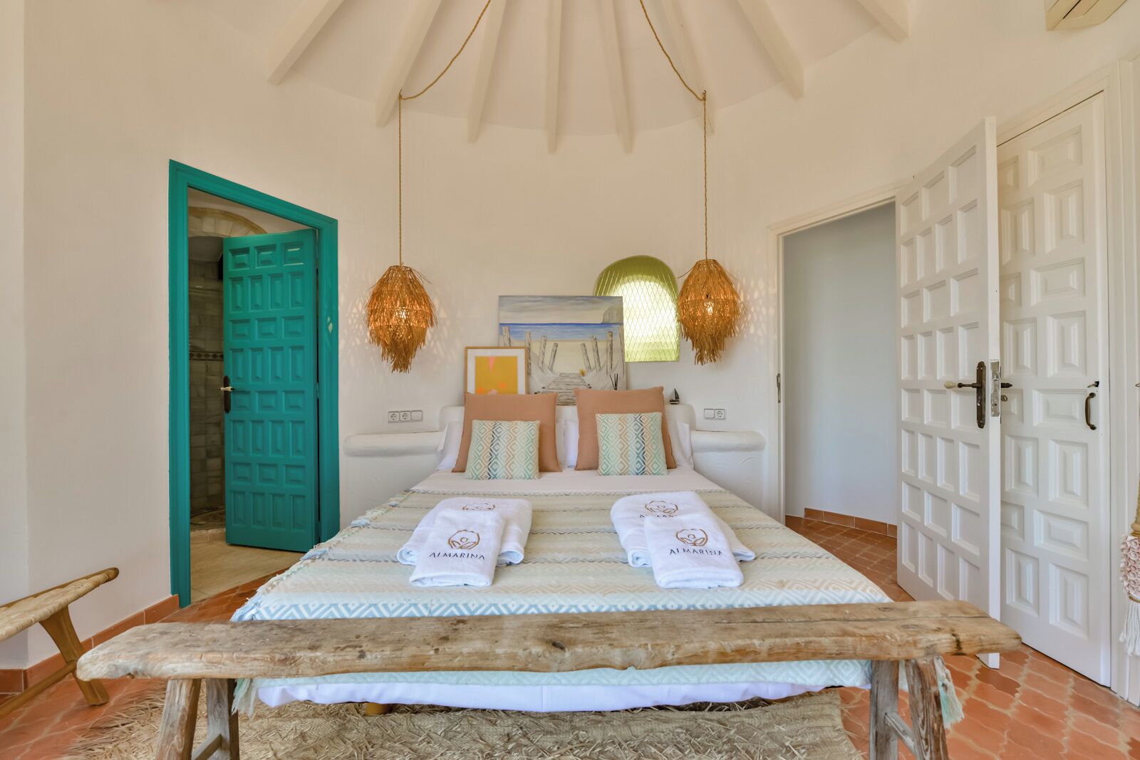 A bedroom with a bed, two hanging lamps, a wooden bench, and a teal door.