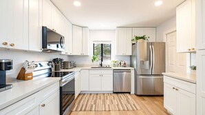 Une cuisine moderne avec des meubles blancs, des appareils électroménagers en acier inoxydable et un plancher en bois.