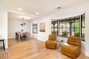 A spacious living area with a dining table, two leather armchairs, and large windows offering a view of the outdoors.