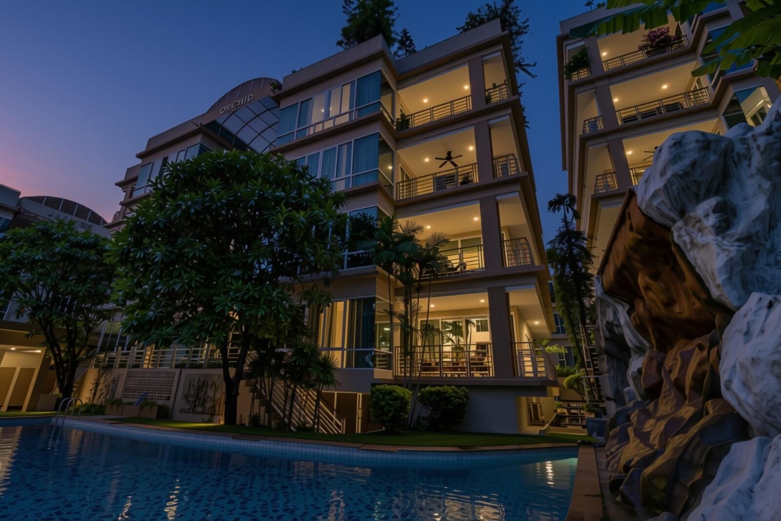 A multi-story hotel with balconies, a swimming pool, and a rock formation.