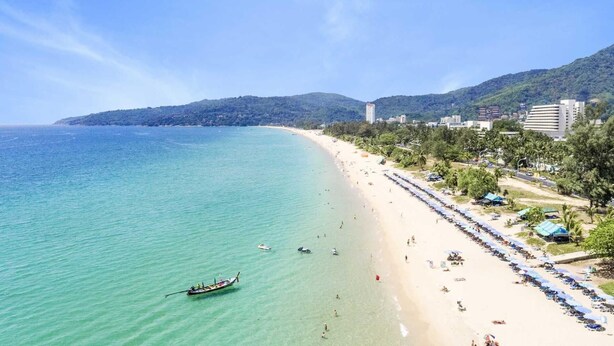 Una platja amb aigües turqueses cristal·lines, filera de sombrerets i un vaixell a l'aigua.