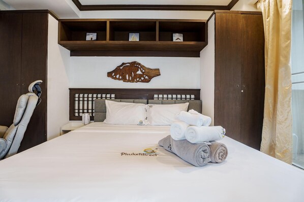 A neatly made bed with rolled towels, a wooden headboard, and a wall-mounted shelf with framed pictures. - 4.13 Karon View 2 Bed, 5 Minutes walk Karon Beach (Karon)
