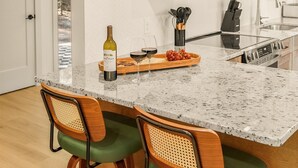 A kitchen with a granite countertop, two bar stools, a wine bottle, and a fruit bowl. - Family Base Camp + 5BR + Game Room + Hot Tub (McGaheysville)